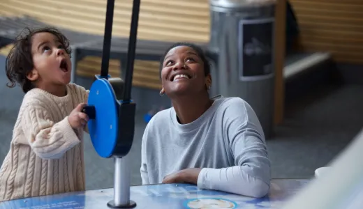 A child playing with a parachute exhibit and looking up in awe with their adult next to them smiling