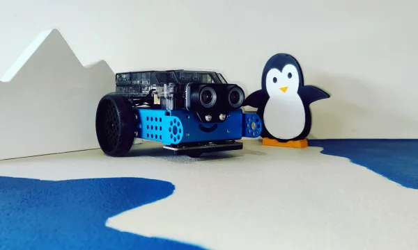 a blue mBot robot with a penguin to it's right 