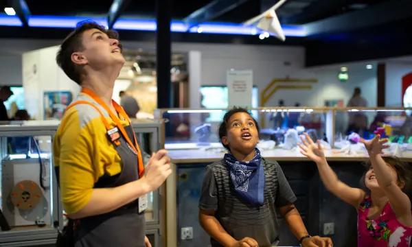 An adult and a child are in a science centre looking up at a piece of paper hovering in the air.