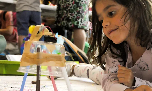 A small child is lying on the floor next to a creation made with a circuit and pens.