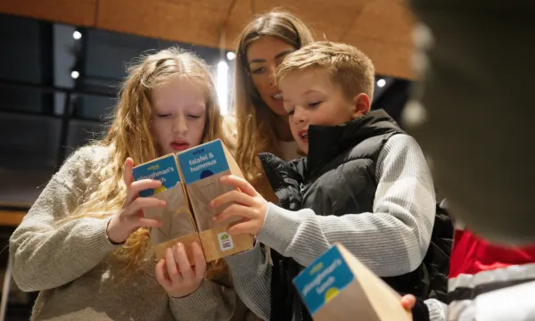 Two children and an adult hold sandwich packaging to read the labels