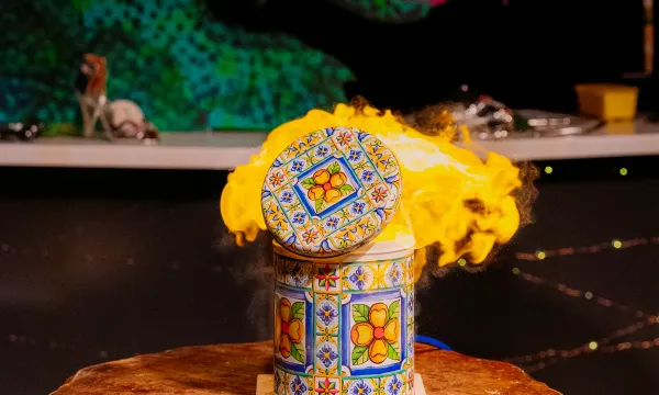 A dragon is in the background of the image with it's mouth open. In the foreground is a bright yellow flame. Taken from a demonstration from Fariytale SOS studio show at We The Curious