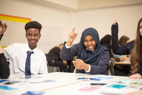 Students around a table smiling and raising their hands