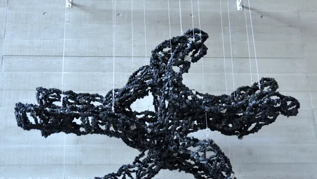 A large sculpture made of black chains, suspended from a white frame 