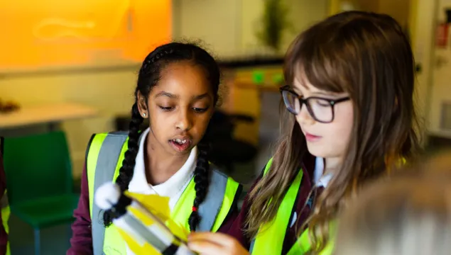 Two children in high-vis vests looking concentrated whilst putting together a rocket 