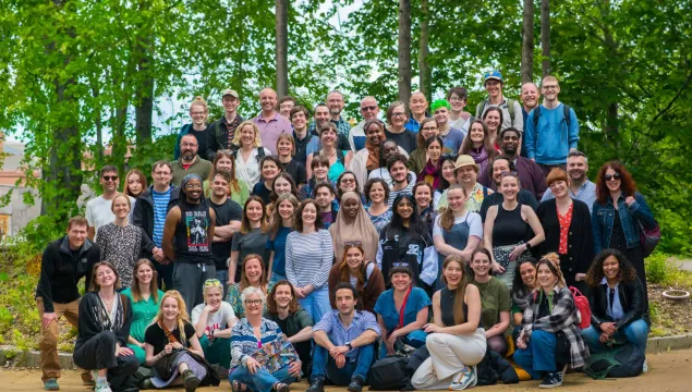 A large group photo featuring approx 100 people looking towards the camera, with green trees behind them