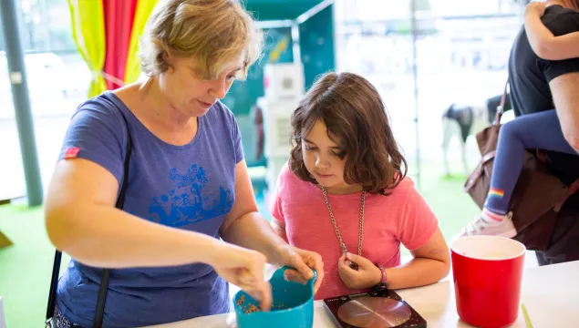 An adult and child are together in a kitchen space with a brightly coloured bowl on a white surface. 