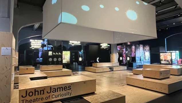 A space with wooden box-like seating and an elevated cube projector screen