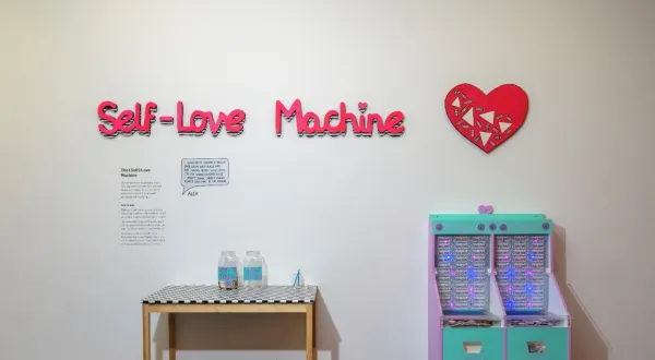 An artwork entitled 'Self-Love Machine' with a coin-slot game in bright colours