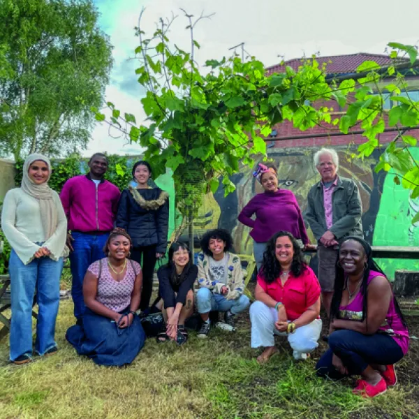A group of people in front of some plants, together for a photo. Some are crouched, some are stood up.